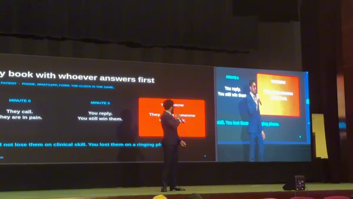 Moiz Khurram presenting the patient booking timeline across the conference's twin screens.